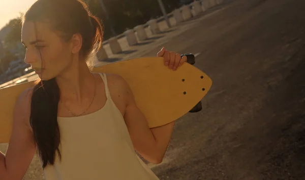 女孩与 skatedoard 在她的肩膀在夏天看的距离 — 图库照片