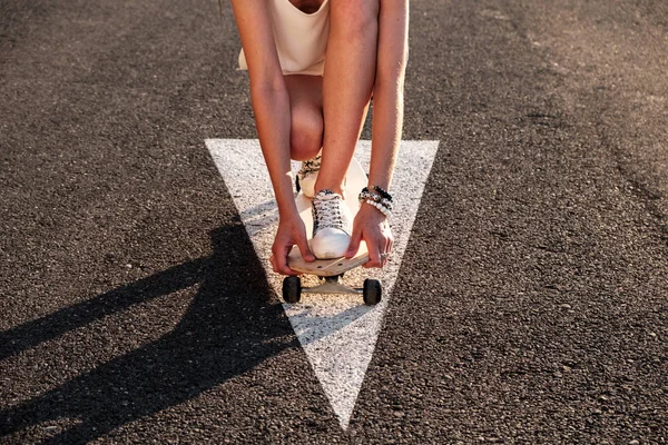 Chica patinadora sentada a bordo en la calle en el camino de flecha marcado retroiluminado por la luz del atardecer — Foto de Stock