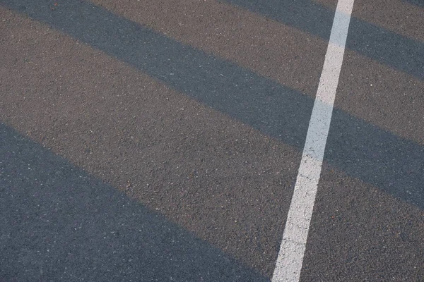 Trafikkledning malt over ny asfaltflate på vei med solnedgangsmønstre som skinner gjennom bygning – stockfoto
