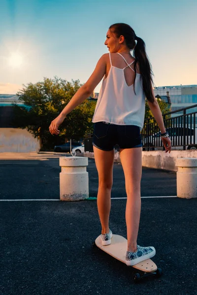 Mooi meisje paardrijden skateboard in het kort denim shorts, uitzicht vanaf de achterkant — Stockfoto