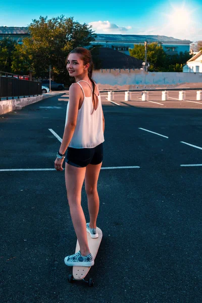 Achterzijde bekijken van jong meisje in het kort denim shorts met lange blote benen en lange haren in paardenstaart paardrijden skateboard — Stockfoto