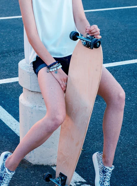 女孩坐在滑冰公园与她的长板在她裸露的腿之间 — 图库照片