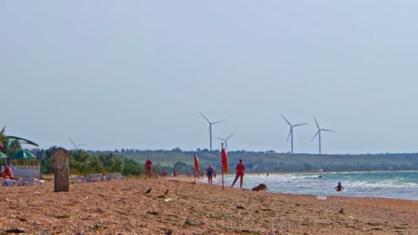 Onherkenbaar mensen op het strand voor het werken van windturbines — Stockvideo