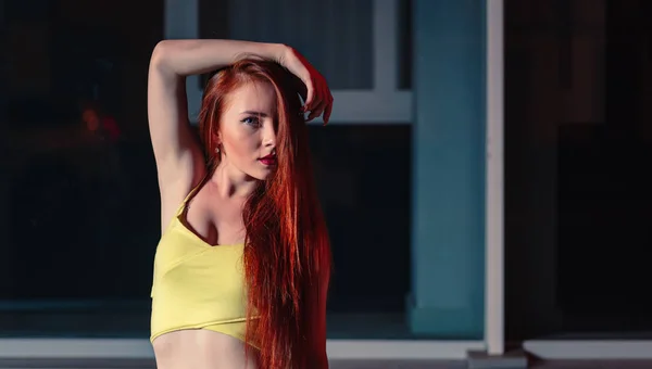 Chica pelirroja, retrato en la ciudad nocturna. Calle estilo retrato de la moda de la joven mujer bonita con el pelo largo y rojo con camiseta amarilla posando con media cara oculta por el pelo — Foto de Stock