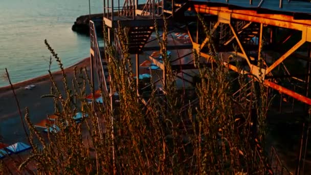 Blick auf den Badeort von oben mit eiserner Treppe nach unten und trockenem Sommergras, das im Wind zittert — Stockvideo