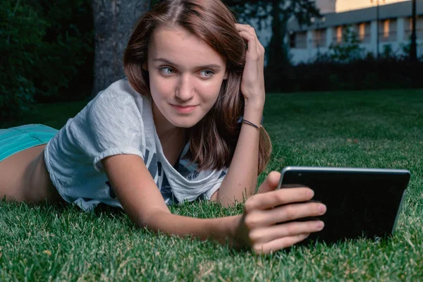 Młoda dziewczyna użytkownik komputera typu tablet leżącej trawa zielony park i flirty — Zdjęcie stockowe