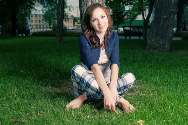 Молодая девушка сидит скрестив ноги на весенней траве улыбаясь — стоковое фото