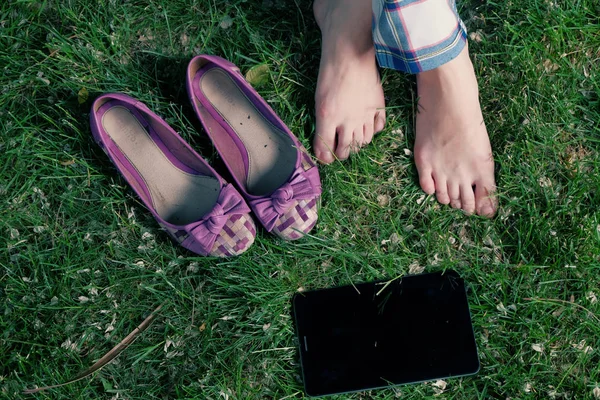 赤脚妇女她的鞋和平板电脑在草地上 夏季休息 — 图库照片