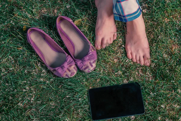 女孩坐在草地上盘腿与她的鞋子和平板电脑附近, 顶视图 — 图库照片