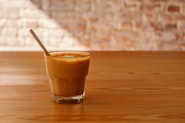 Flat white coffee in transparent glass on table in cafe. It is espresso-based coffee drink consisting of espresso with microfoam steamed milk with fine bubbles with a glossy or velvety consistency