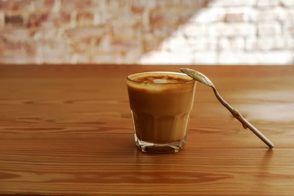 Flat white coffee with spoon on wooden table. It is espresso-based coffee drink consisting of espresso with microfoam steamed milk with small bubbles with a glossy or velvety consistency.