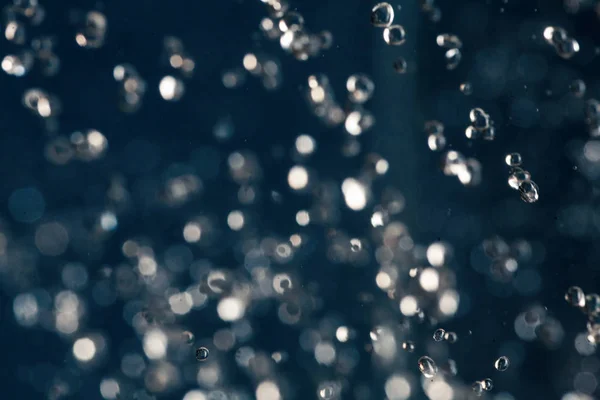 Gotas desenfocadas de agua vuelan sobre fondo azul profundo — Foto de Stock