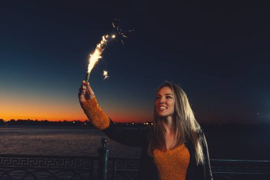 Karanlık gece gökyüzü önünde yükseltilmiş yükseltilmiş elinde maytap yanma ile mutlu kadın