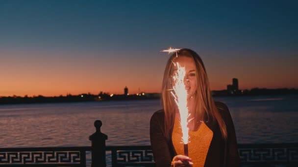照明の花火と日没で自由を楽しんでいるブロンドの髪の女性。楽しくカラフルな空を見上げて花火を保持している女性 — ストック動画