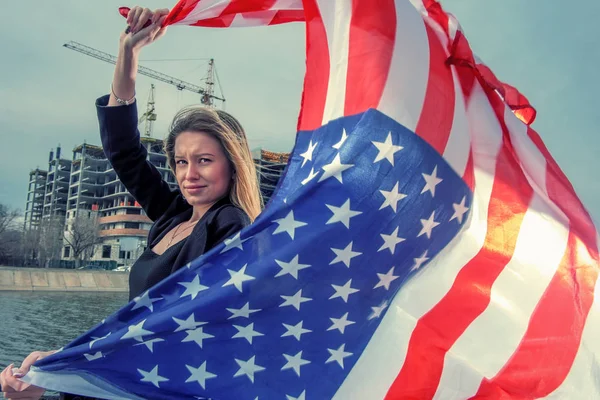 Uma bela jovem segurando uma bandeira americana voar pelo vento — Fotografia de Stock