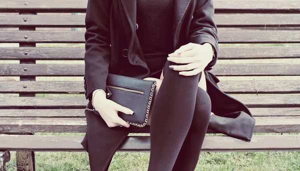 Модний підліток тримає чорну зчеплення, сидячи на лавці парку у весняний час. стилі Instagram — стокове фото