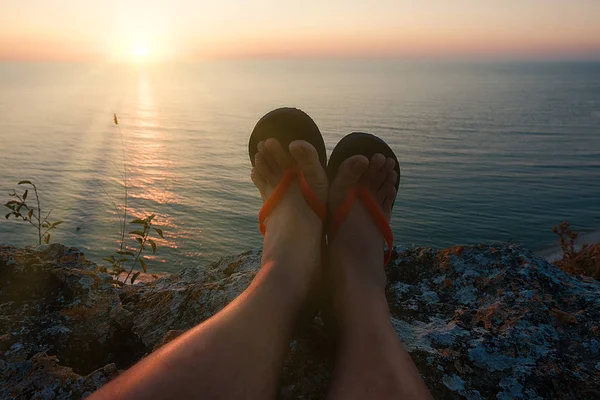 Vista POV delle gambe uomo in infradito sulla scogliera alta davanti al sole al tramonto — Foto Stock