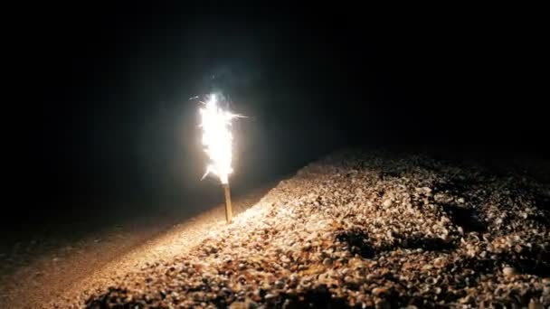 Sparkler ardiendo en el borde del agua en la playa — Vídeo de stock