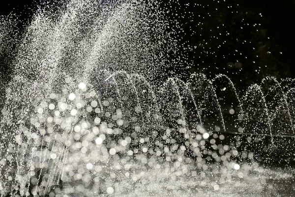 Chorros de agua de la fuente en el parque parcialmente borrosa fondo bokeh — Foto de Stock