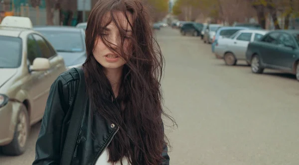 Fille dans la journée venteuse avec des cheveux soufflés dans la rue avec des voitures garées — Photo