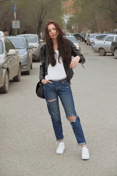 Sad woman in jeans posing with handbag in the center on the street