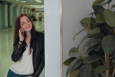 Genç bir kadın hareket halindeyken telefon eder ve duvardan duvara eğilerek mutlu bir şekilde konuşur.