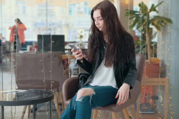 Концентрована дівчина-хіпстер дивиться на смартфон під час онлайн-відеодзвінка, сидячи в кав'ярні. Весела ділова жінка проводить конференцію в Інтернеті — стокове фото