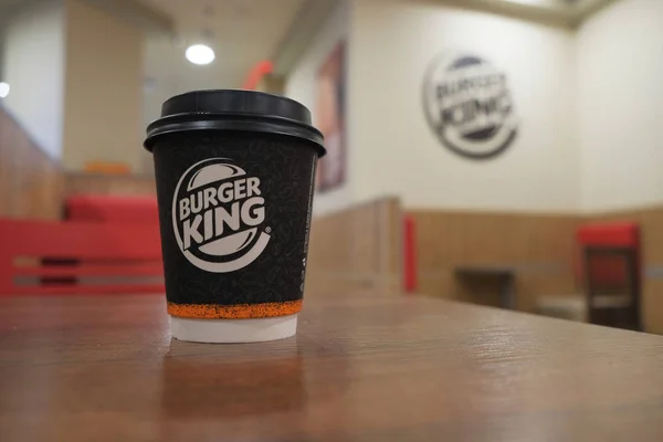 Astrachan, Rusland-15 april 2019: Burger King koffie-to-go afhaalmaaltijden kopje op tafel bij wazig restaurant achtergrond. Burger King is een wereldwijde fastfoodketen die hamburgers, frietjes, desserts en — Stockfoto