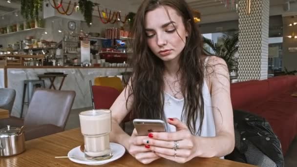 Astrachań Rosja-20 kwiecień 2019: młoda dziewczyna siedzi w kawiarni za pomocą telefonu komórkowego iPhone — Wideo stockowe