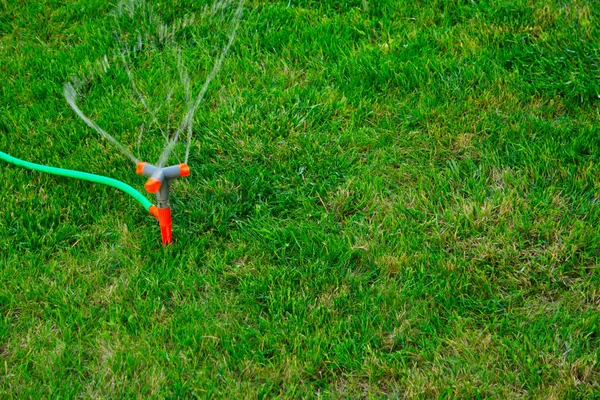 Aspersor móvil sobre hierba. Aspersor chorros de rociado de agua en la hierba verde exuberante con espacio de copia — Foto de Stock