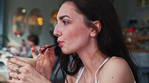 Serious girl drinks coffee from transparent glass with straw — Stock Video