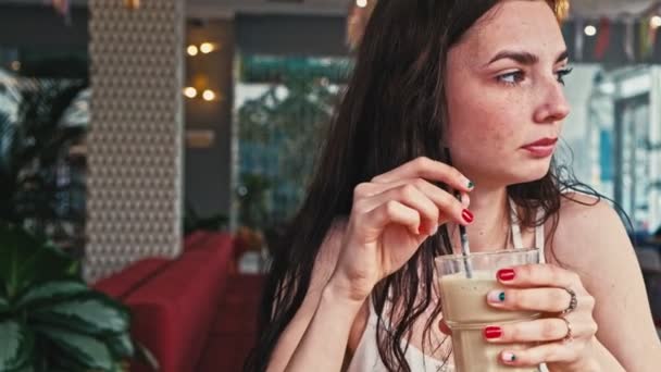 Serious girl drinks coffee from transparent glass with straw front view — Stock Video