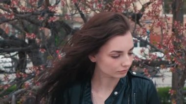 Sakin kız arka planda çiçek açan kiraz ağacı ile rüzgarlı bir günde parkta poz