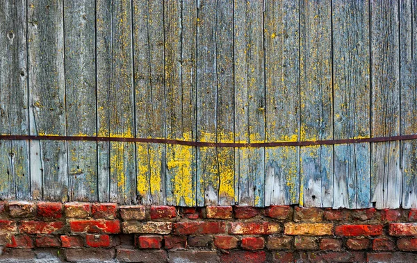 Старый деревянный забор стоит на фундаменте из красного кирпича — стоковое фото