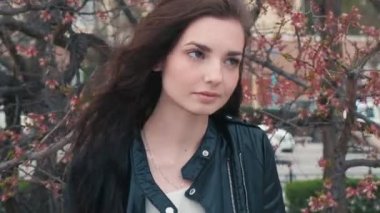 Siyah kiralık ceketli havalı kız kiraz ağacının önünde poz veriyor.