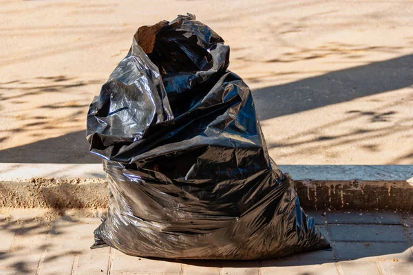 Bolsa de plástico negro con residuos domésticos cerca de la acera en la calle — Foto de Stock