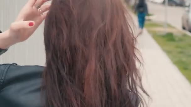 Achteraanzicht van een mooi jong meisje met lang bruin haar dat buiten een sigaret rookt. Een mooie jonge brunette met lang haar roken in de straat bij winderig weer real-time beelden — Stockvideo