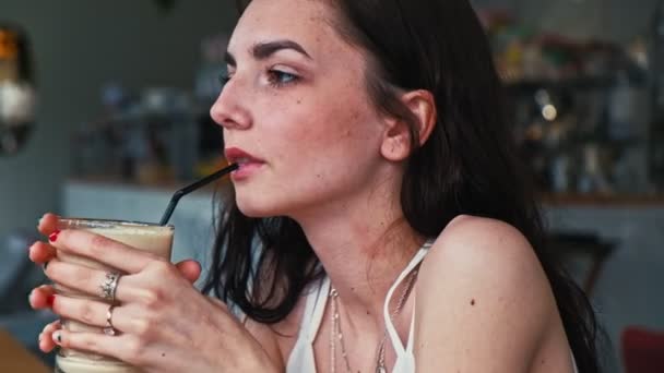 一个年轻的女人在咖啡馆里喝着稻草咖啡 — 图库视频影像