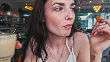 Küçük boy kurabiye yiyen genç bir kadının yüz görüntüsü.