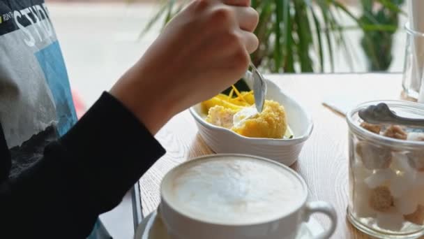 Garçon manger frit-glace dessert dans un café avec cuillère avec tasse de café à côté de lui — Video