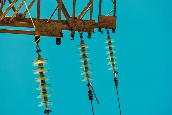 Sada elektrických izolátorů s dráty namontovaných na rezavě energetické věži před modrým nebem — Stock fotografie