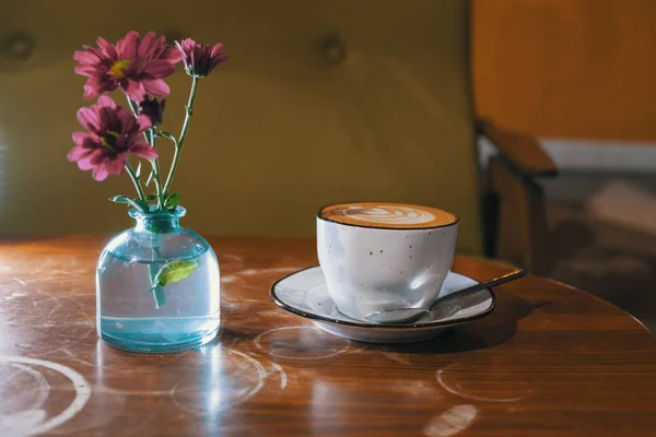 Blumen in einer Flasche blauer Farbe auf der Tischplatte und einer Tasse Kaffee — Stockfoto