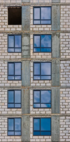 Pionowy rząd okien budynku apartamentowego w stanie rozwoju z refleksjami błękitnego nieba w szklance okiennej — Zdjęcie stockowe