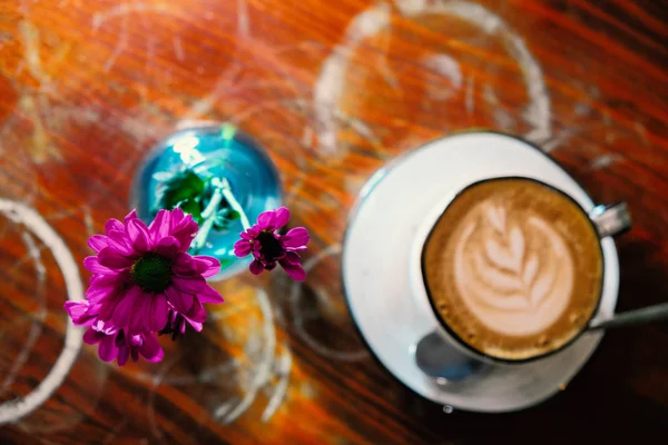 Cappuccino copo na mesa wih flores em garrafa azul vista superior — Fotografia de Stock