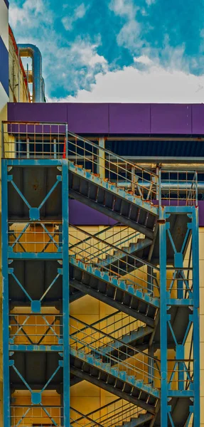 Um bloco de apartamentos de concreto alto com repetindo escadas de escada de incêndio externas com grades de metal e um céu azul — Fotografia de Stock