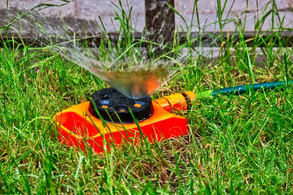 Garden sprinkler of orange color working on lawn with fountain of water in an air — Stock Photo, Image