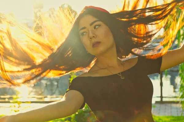 Aziatisch meisje schudt haar haar in een zomerpark. Buiten Vintage kleur. Achtergrondverlichting portret van jonge vrouw met vliegende blazen haar schijnt in de zon. — Stockfoto