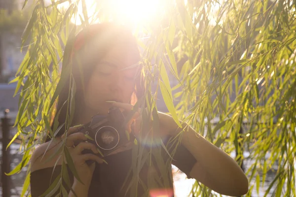 Háttérvilágítással elmosódott alacsony kontraszt ázsiai lány kamerával a parkban naplementekor. Barna lány filmes fényképezőgép a szüreti kép — Stock Fotó