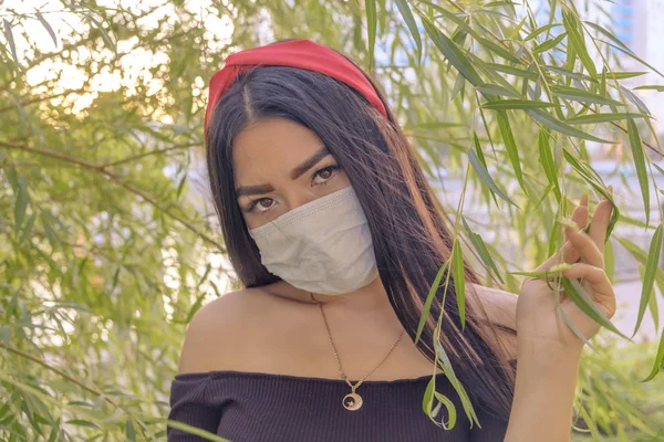 Asian woman wear face mask while posing in the park against willow branches