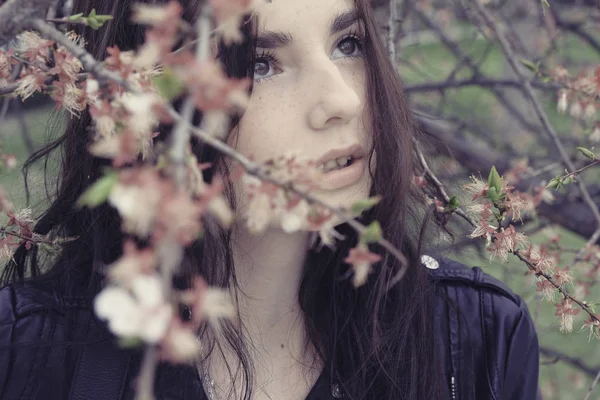 Pensive girl hiding in cherry flower branches looking up — Stockfoto